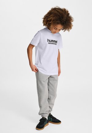 Hvid bomulds t-shirt med "hummel" logo i sort, parret med grå sweatpants og sorte sneakers med grønne detaljer og gul branding.
