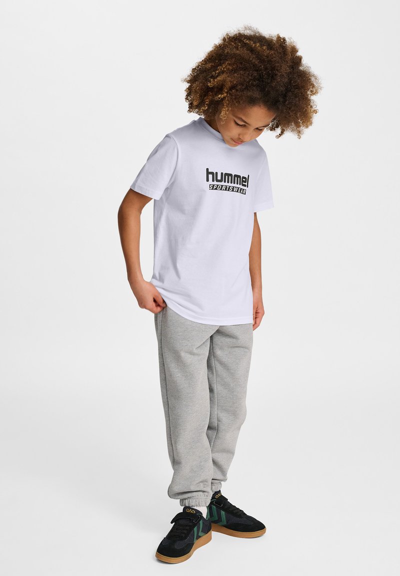 Vit bomull t-shirt med "hummel"-logotyp i svart, kombinerad med grå sweatpants och svarta sneakers med gröna detaljer och gul branding.