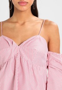 Punavalkoraidallinen olkapäät paljastava toppi, jossa ohuet olkaimet, nyppätty kangas pääntiellä ja väljähkö istuvuus. Valmistettu tekstuurillisesta, kevyestä puuvillasekoitteesta.