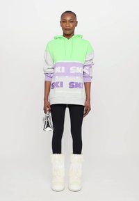 Colorful oversized hoodie in green, gray, and lavender with "SKI" print; paired with black leggings and white fur-lined boots. Silver handbag.