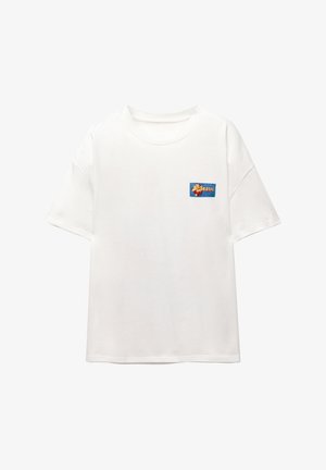 Bijela pamučna majica s opuštenim krojem i kratkim rukavima, na kojoj se nalazi šarena grafika "BRASIL" na plavom uzorku na lijevoj strani prsiju.