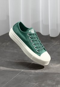 Grønne kanvas lave sneakers med en hvit gummisåle, teksturerte luftehull og avrundet tå. Har et logopatch på tungen.