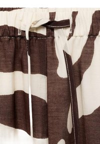 Tessuto a motivo marrone e crema con vita elasticizzata. Il tessuto ha una consistenza scorrevole con dettagli di design a pieghe fluenti.