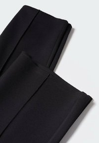 Zwarte op maat gemaakte broek van een gladde stof, met een plooi aan de voorkant, netjes gevouwen met een platte tailleband.