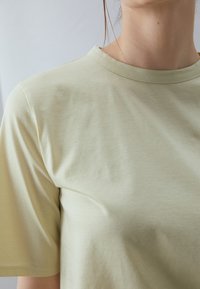 Tricou scurt cu mânecă scurtă, de culoare verde deschis, confectionat dintr-un material moale, având un decolteu rotund și o textură netedă fără modele sau accente vizibile.