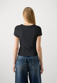 Svart topp med korte ermer, rund hals, tettsittende design og glatt tekstur, kombinert med høyhalsede blå denimjeans med baklommer.