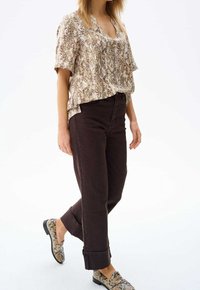 Ljusbrun, kortärmad topp med ormskinnsmönster, parat med mörkbruna raka jeans och skor med ormskinnsmönster. Avslappnad passform.