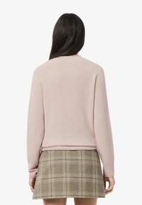 Ljusrosa tröja i mjukt material med ribbade muddar, i kombination med en rutig kjol i olika nyanser av grönt och beige.