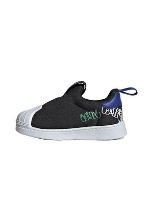 Zapatilla negra sin cordones con puntera de goma blanca, detalles de grafiti en blanco y verde, lengüeta azul en el talón y suela blanca sobre fondo blanco.