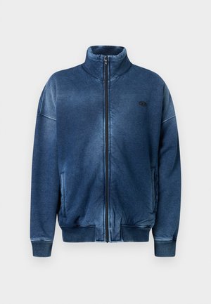 Chaqueta azul con cremallera hecha de tela suave, con cuello alto, puños acanalados, bolsillos laterales y un logo bordado en el pecho.