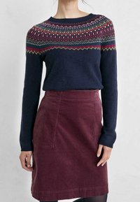 Pull en maille bleu marine avec un empiècement géométrique multicolore, associé à une jupe en velours côtelé bordeaux. Le pull possède des manches longues et un col rond.