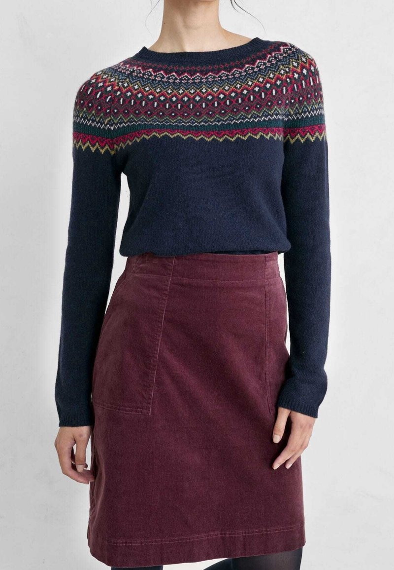 Pull en maille bleu marine avec un empiècement géométrique multicolore, associé à une jupe en velours côtelé bordeaux. Le pull possède des manches longues et un col rond.