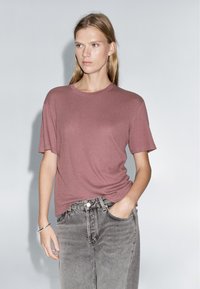 Short-sleeve, crew-neck t-shirt in muted rose, made from soft fabric. Paired with high-waisted, faded gray denim jeans.
