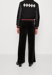 Svart bomberjacka med läderärmar och broderad "GUESS"-logotyp. Svarta sammet brett benbyxor med en slät yta, ihopparade med skor med blockklack.