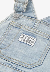 Poche de salopette en denim bleu clair avec une étiquette blanche Levi Strauss & Co. et une boucle de sangle réglable en métal argenté.
