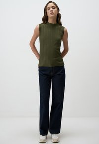 Top senza maniche verde oliva con pieghe verticali, abbinato a jeans a gamba larga blu scuro e scarpe da ginnastica chiare. Texture liscia, design minimalista.