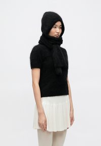 Top negru, tricotat, cu mâneci scurte, puțin pufos, asortat cu o fular și o glugă din același material. Modelul poartă o fustă ușoară plisată și colanți.