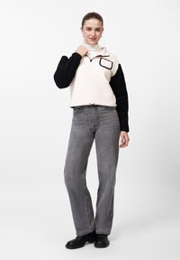 Φλις πουλόβερ σε κρέμα και μαύρο με φερμουάρ στο λαιμό, μπροστινή τσέπη, σε συνδυασμό με γκρι τζιν ψηλόμεσο και μαύρες μπότες.