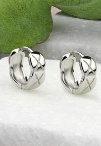 Silvriga hoopsörhängen med en polerad yta, med en slät, böjd design och ingraverade 'X'-accenter framtill.