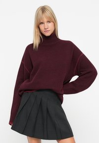 Burgundská oversized roláková mikina s textúrovaným pletením, skombinovaná s čiernou sukňou s plisovaním s vysokým pásom.