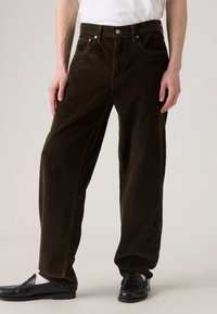 Pantaloni din corduroy de culoare verde măslin închis, cu un design cu picior larg, cinci buzunare și un material texturat cu nervuri verticale.