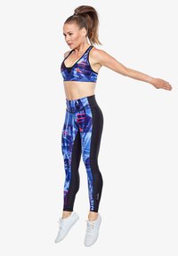 Sportbh en leggings set in blauw en zwart met abstracte patronen. Gemaakt van rekbaar materiaal, met een hoge taille. Witte schoenen.
