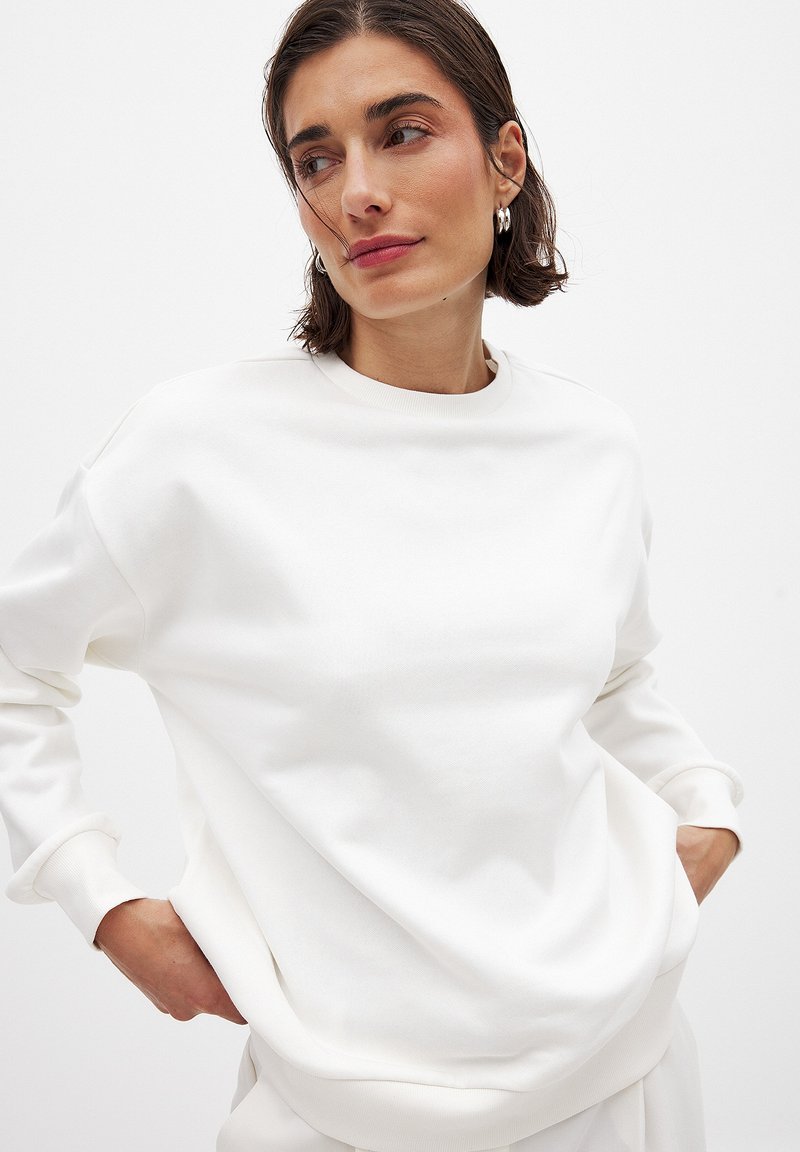 Witte sweatshirt met een ronde halslijn en lange mouwen, met een relaxte pasvorm en zachte textuur. De mouwen en de onderkant zijn ribgebreid.