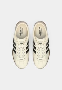 Λευκά δερμάτινα αθλητικά παπούτσια με τρεις μαύρες ρίγες στα πλευρά, στρογγυλεμένη μύτη και υφασμένο λαστιχένιο πέλμα με κλείσιμο με κορδόνια.