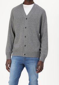 Cardigan gris de punto con escote en V, cierre frontal de cinco botones, puños y dobladillo acanalados, llevado sobre una camisa blanca y combinado con jeans azules.
