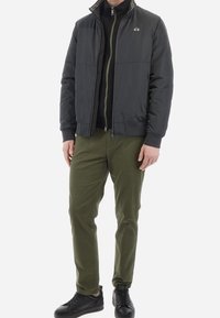 Prošívaná, tmavě šedá bomber bunda s černými detaily, zapínání na zip a stojáčkový límec; v kombinaci s olivově zelenými kalhotami a černými teniskami.