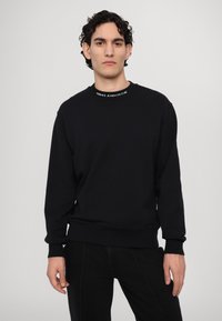 Sweatshirt in cotone nero con maniche lunghe, collo rotondo e polsini a coste. Presenta il logo "VERSACE JEANS COUTURE" in bianco sul colletto.