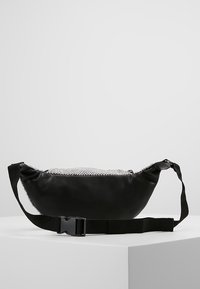 Marsupio in pelle nera con parte superiore in rete decorativa argentata, forma curvata, cintura regolabile e chiusura con fibbia in plastica.