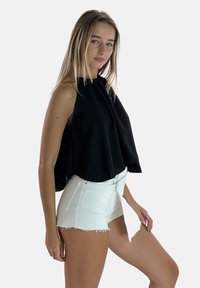 Schwarzes ärmelloses Oberteil mit hohem Kragen und fallendem Design. Kombiniert mit weißen Denim-Shorts mit ausgefransten Säumen und tailliertem Bund.