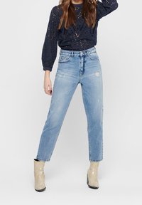 Světle modré džíny s vysokým pasem a rovnými nohavicemi. Kombinované s tmavě modrým perforovaným svetrem a béžovými kotníkovými botami.