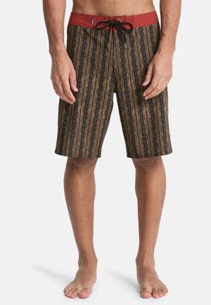 Zwemshort met een rode tailleband en zwarte trekkoorden, met een meerkleurig geometrisch patroon op een bruine achtergrond. Ontwerp tot op de knieën.