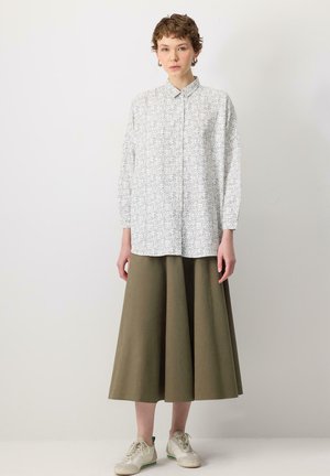 White floral shirt with a collar and long sleeves, paired with a knee-length olive green skirt and light sneakers.