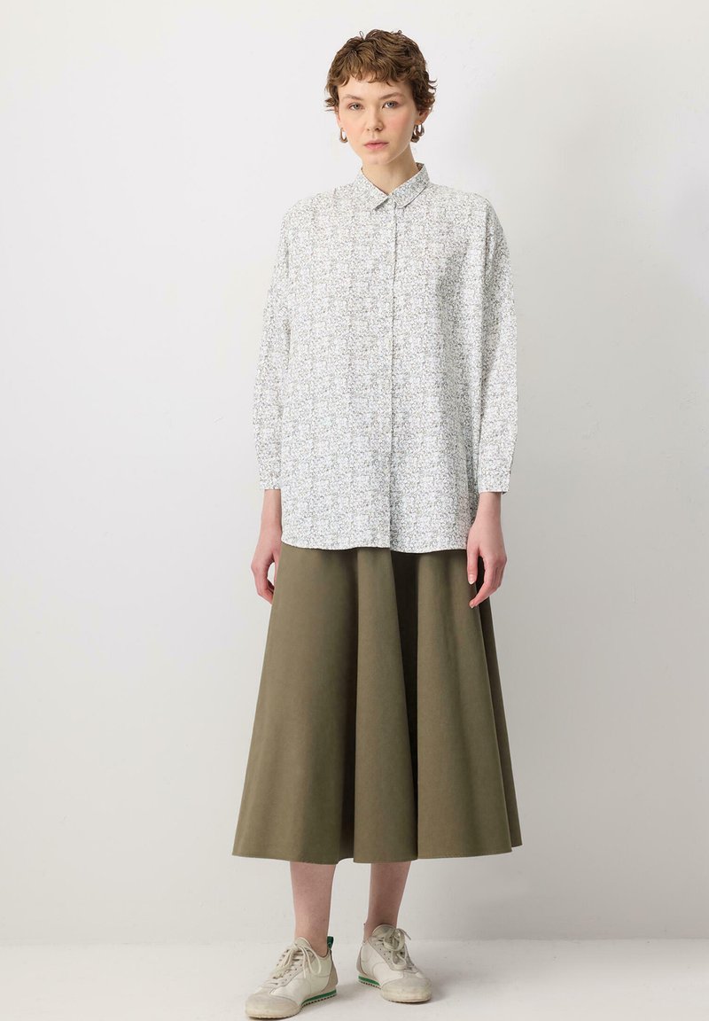 White floral shirt with a collar and long sleeves, paired with a knee-length olive green skirt and light sneakers.