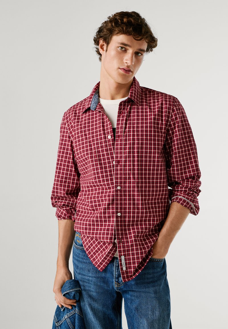 Camicia a quadri rossi e bianchi con colletto in denim a contrasto. Maniche lunghe arrotolate, abbinata a jeans in denim blu.