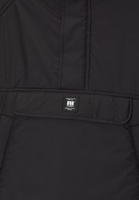 Giacca nera imbottita con una texture liscia, caratterizzata da una toppa con logo sulla tasca frontale e dettagli cuciti.