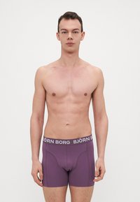 Lila boxer alsónadrág puha anyagból, fehér logós derékpánttal. Fitted kialakítású és sima textúrájú, kényelmet és támaszt nyújt.