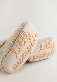 Chaussons pour bébés en tricot beige avec semelles douces, portant un texte orange en relief "petite citrouille" sur un fond clair.