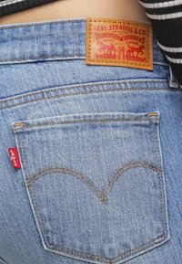 Ljust blå denimjeans har en läderlapp märkt "Levi Strauss & Co." och en röd etikett på bakfickan med ikonisk sömnadsdetalj.