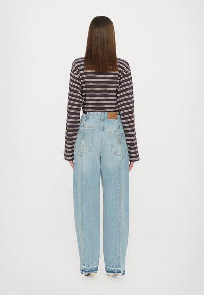 Stripet langærmet top i mørk lilla og creme, kombineret med lys blå vide ben jeans med ryglomme detaljer og en læderpatch.