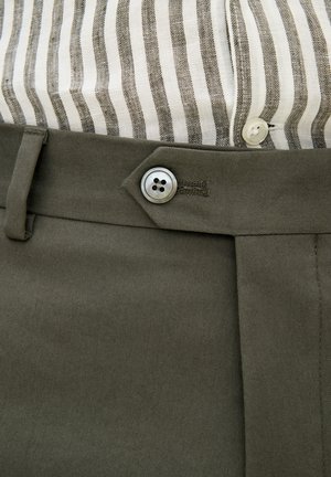 Pantalons en coton vert olive avec fermeture à bouton, design à l'avant plat et un tissu rayé gris et blanc visible au niveau de la taille.