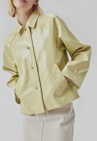 Gelbe, strukturierte Jacke aus Kunstleder mit karierter Musterung, Druckknopfverschluss und Seitentaschen. Verfügt über einen Kragen und eine lockere Passform.