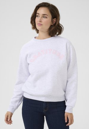Felpa grigia chiara con lettering rosa "GRATITUDE", collo e polsini a costine, tessuto morbido e vestibilità rilassata, abbinata a jeans blu scuro.