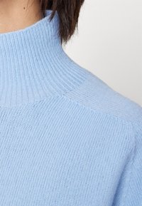Pull à col roulé bleu clair en tissu tricoté côtelé doux, avec un col haut et une conception d'épaule sans coutures.
