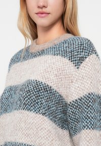 Adīta džemperis ar pārmaiņus svītrām gaismas rozā, zilo un tumši pelēko krāsā. Mīksta tekstūra, apaļa dekoltē un brīva piegriezuma.