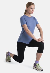 Camiseta atlética azul de manga corta combinada con capris negros, mostrando un ajuste relajado. Llevada con zapatillas grises que presentan acentos en verde y púrpura.