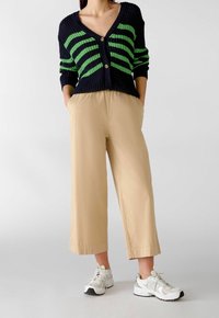 Pletený svetr s námořnickými a zelenými pruhy, s výstřihem do V a dvěma knoflíky, kombinovaný s béžovými zkrácenými kalhotami a bílými sportovními teniskami.